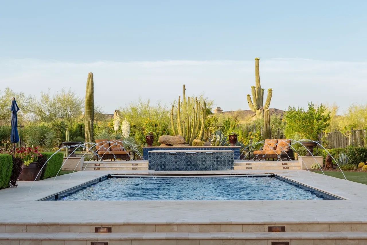 A pool with a fountain and cactus in the background.